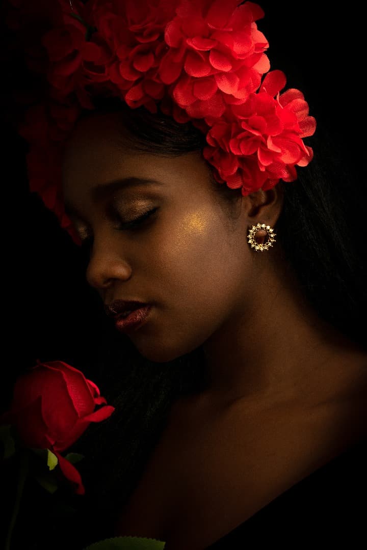 Retrato editorial con flores rojas sobre fondo oscuro